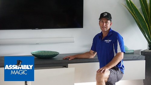 Technician - Ben in front of a floating cabinet he installed. Assembly Magic logo in bottom left corner