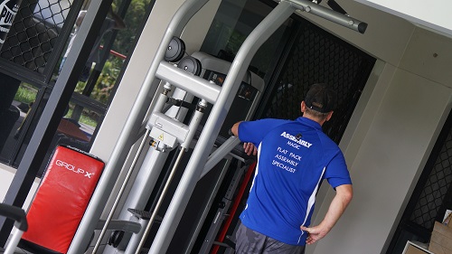 Technician with back facing outwards. Next to some gym equipment he assembled.