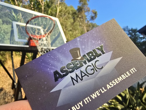 Assembly Magic business card held up in front of a new basketball hoop installation.